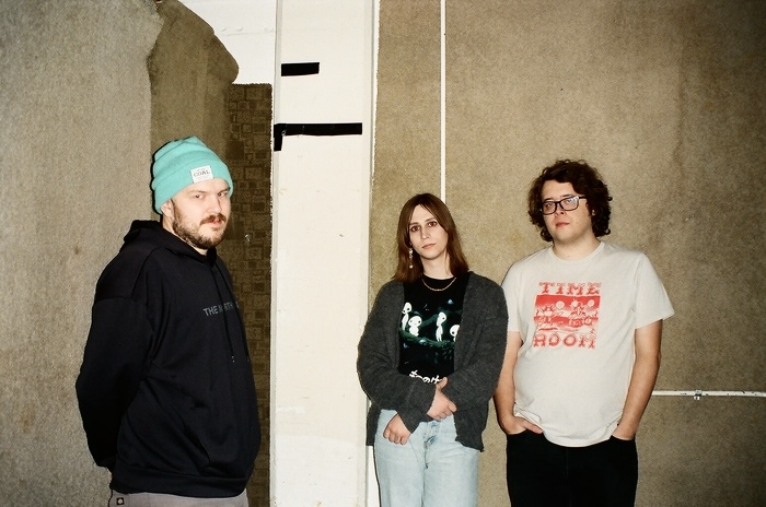 Photo of Malamiko members standing against a carpeted wall.