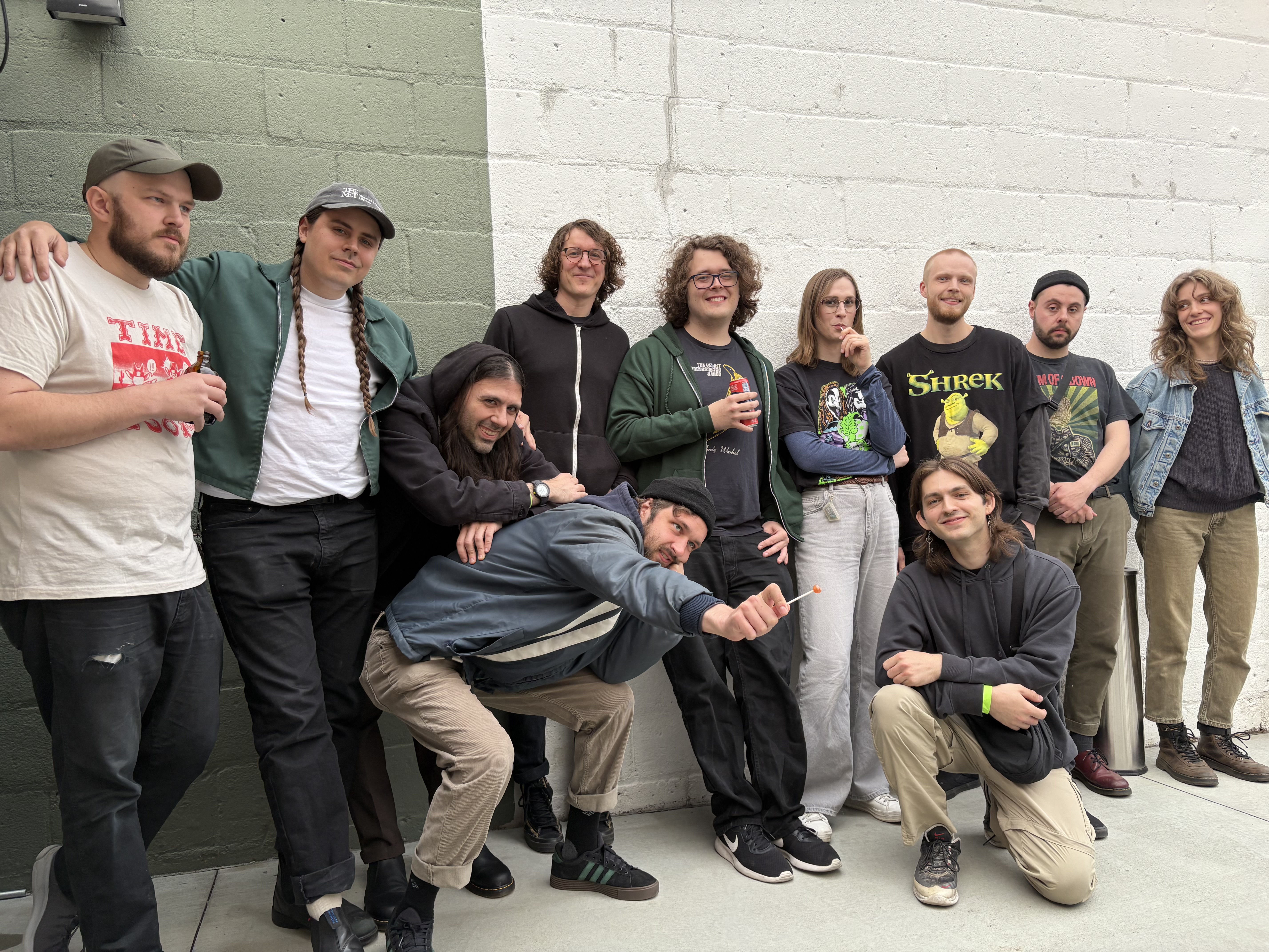 members of malamiko, fend, and another heaven huddled up together in front of a brick wall to celebrate the tour kickoff show